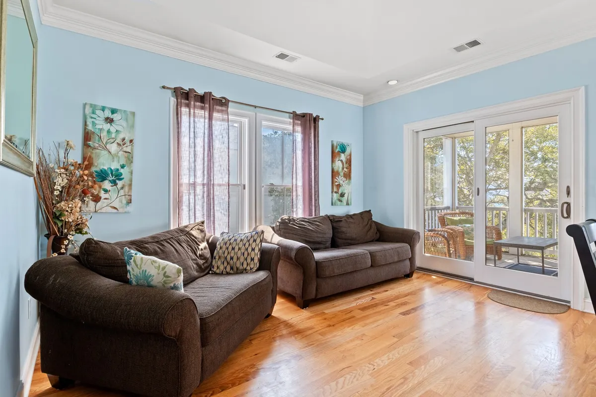 This inviting living room features plush sofas arranged for conversation and relaxation, bathed in natural light from expansive windows. Decorative coastal-inspired paintings adorn the walls, and soft evening lighting creates a warm, welcoming ambiance.