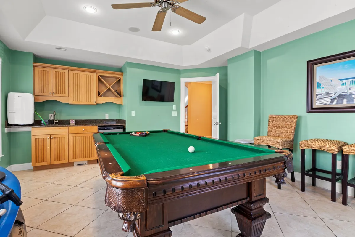 The image spotlights a game room setup with a pool table, wooden cabinetry, and a flat-screen TV prominently displayed. The relaxed and entertaining mood is evident, suggesting a space ideal for watching games, socializing, and celebrating with friends and family.