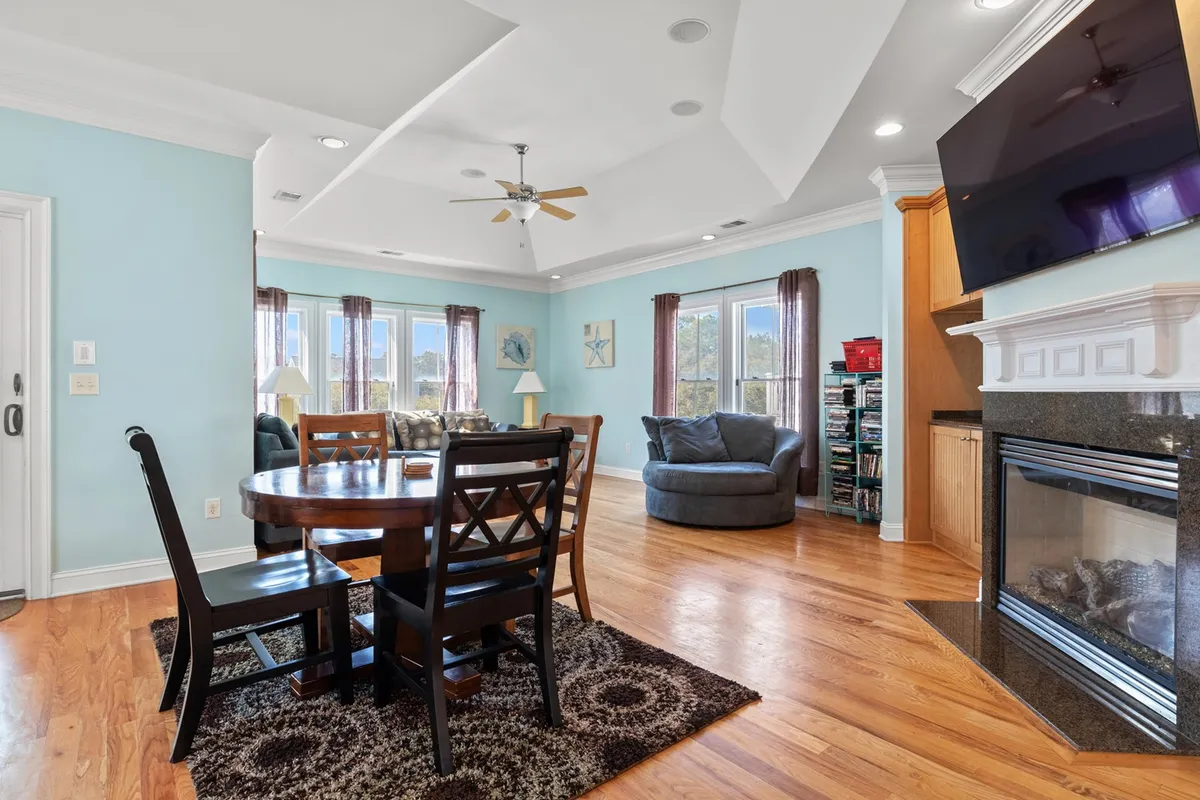 A spacious dining room with a large table surrounded by comfortable chairs, set near a fireplace and large windows that let in ample natural light. The ambiance is cozy and inviting, fitting for shared meals and memorable gatherings.