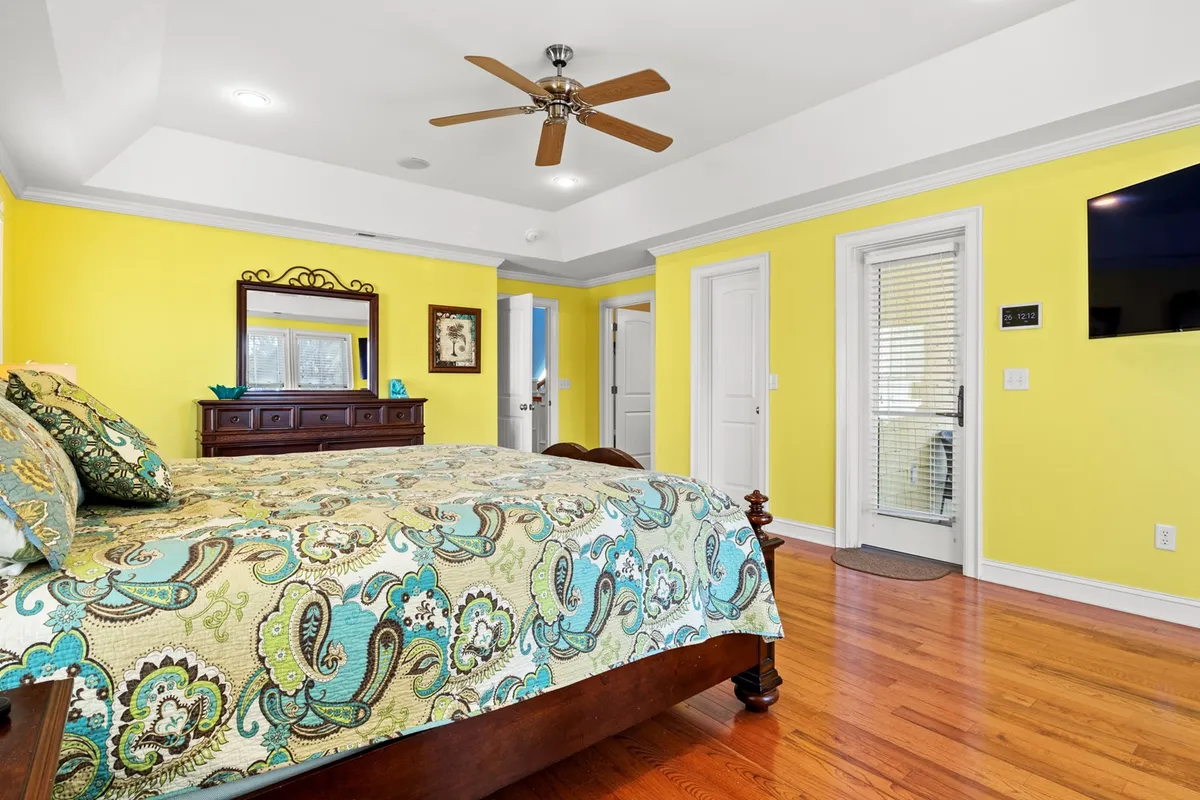 A bedroom with colorful bedding, bright yellow walls, a wooden dresser, and a door that leads outside, blending a lively interior with a subtle connection to the outdoors.