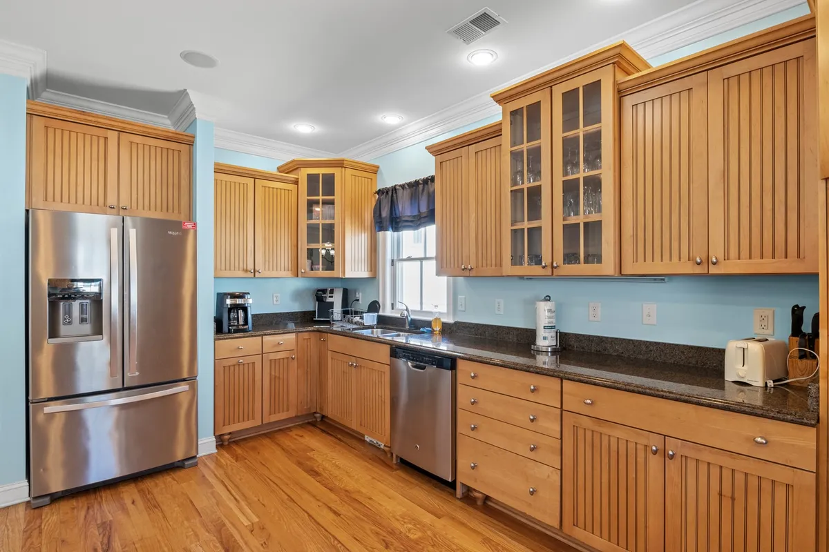 A modern kitchen space featuring a stainless steel refrigerator, granite countertops, ample wooden cabinetry, and a sink positioned below a window. The area is well-lit and ideal for preparing family meals, casual breakfasts, or entertaining guests.
