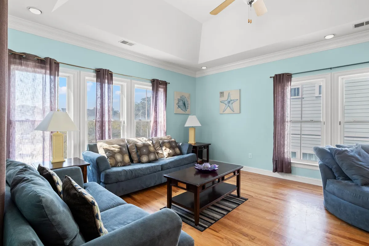 A cozy living area featuring plush sofas arranged around a coffee table, with warm lamps and tasteful decorative art pieces on the walls. Sunlight streams in, creating a welcoming atmosphere ideal for relaxing or entertaining.