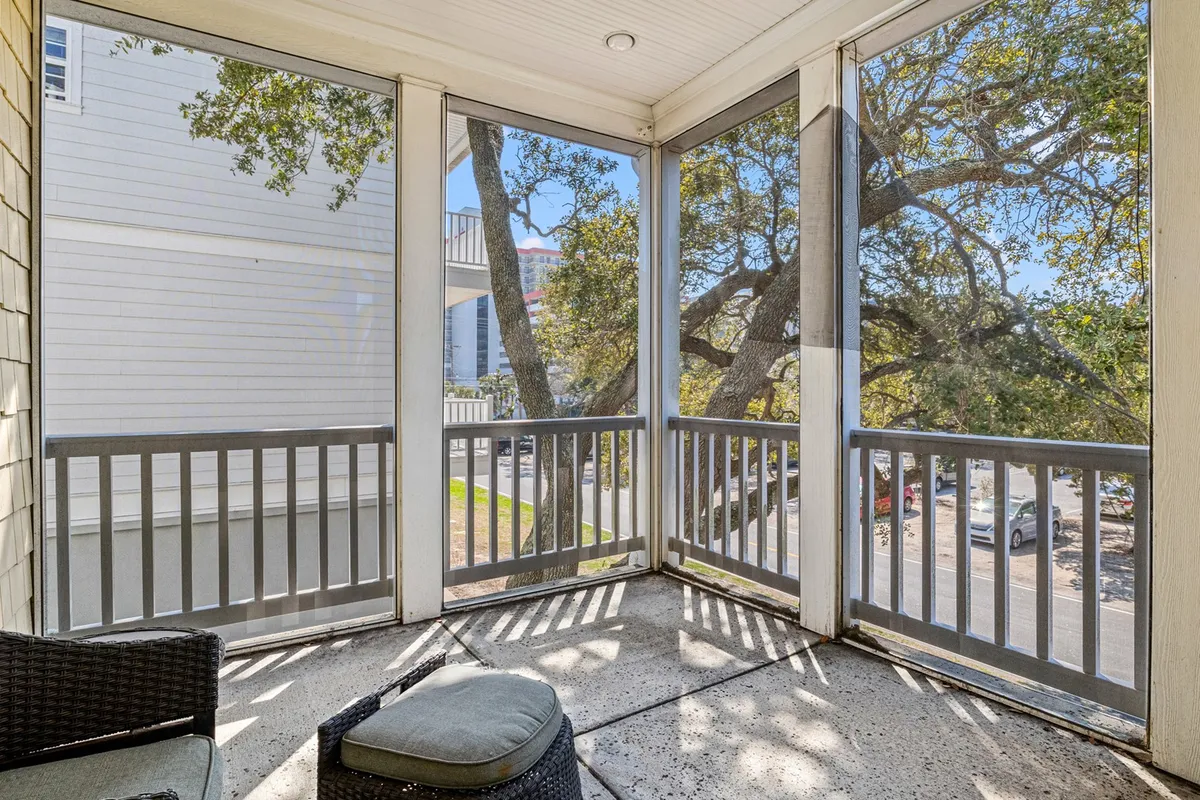 A cozy screened porch nestled among green foliage, furnished for outdoor relaxation. The porch offers a tranquil spot to unwind after a day at the beach, with filtered sunlight and the soothing presence of nature.