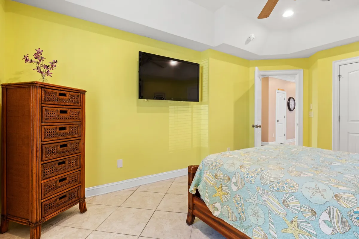 A cozy bedroom featuring cheerful yellow walls, a wooden dresser, and a bed with a patterned cover. Sunlight streams in, creating a bright and welcoming atmosphere ideal for groups to unwind after a day of exploring or golfing.